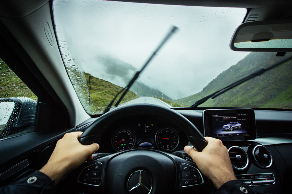 Windshield wipers wiping a wet windshield while hands grip the wheel