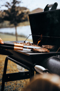Picture of burgers on a grill about to be flipped with a flame rising up at an end of summer BBQ